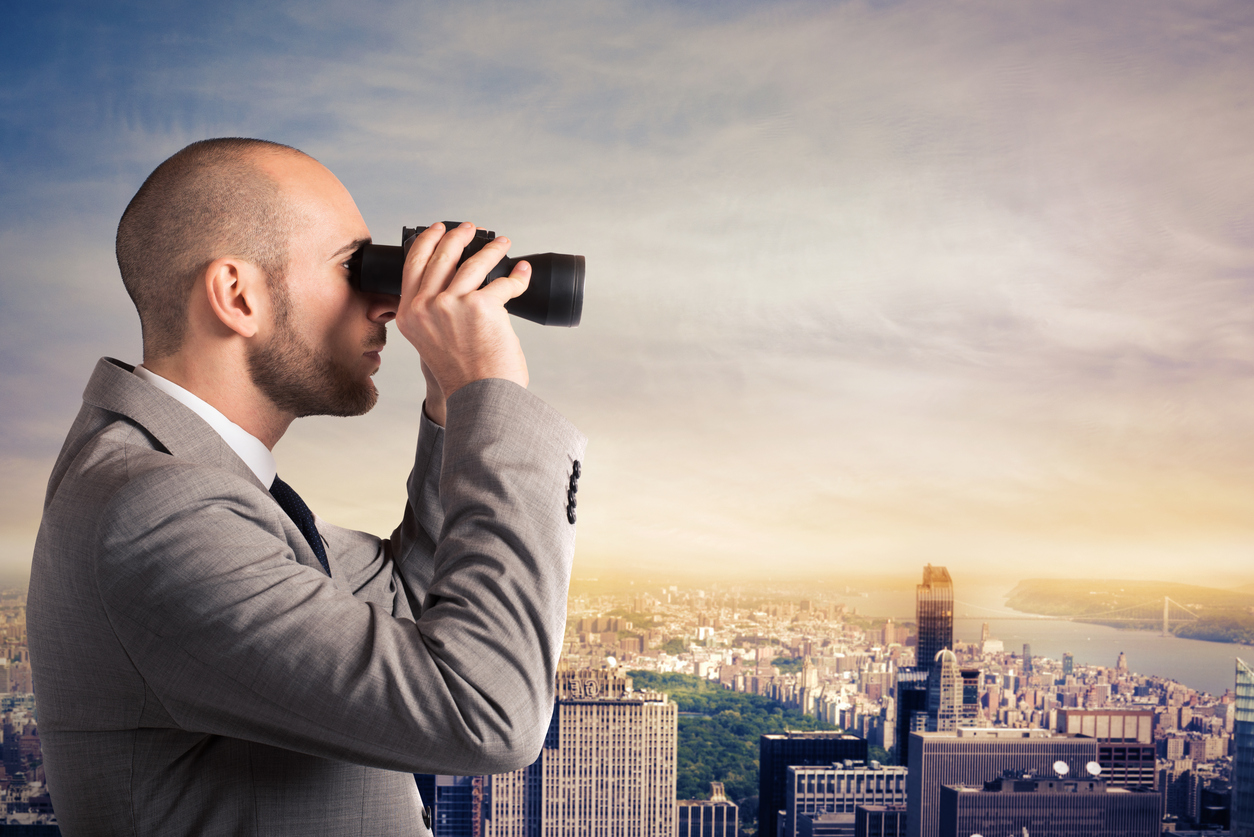 Businessman looks a city landscape with binoculars