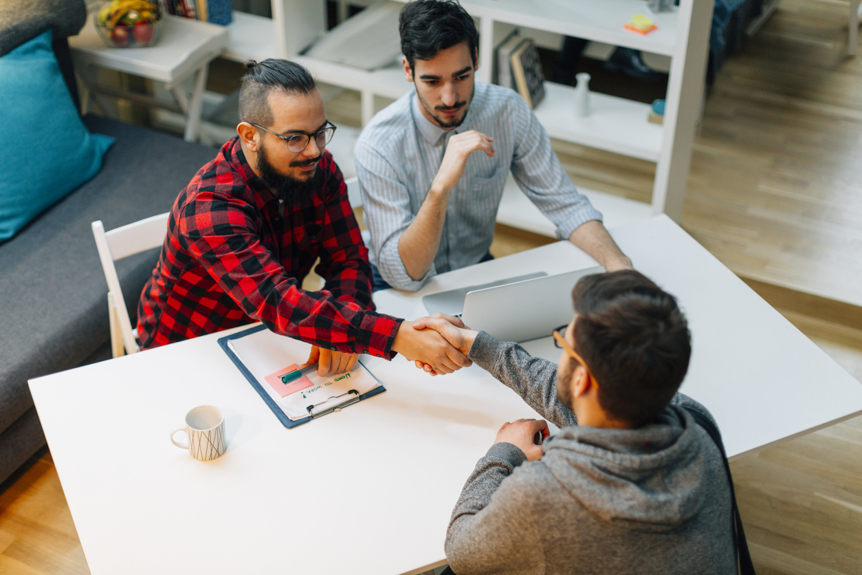 Young man at a job interview talking with two developers. They are running startup developer company from their home. Overhead view.