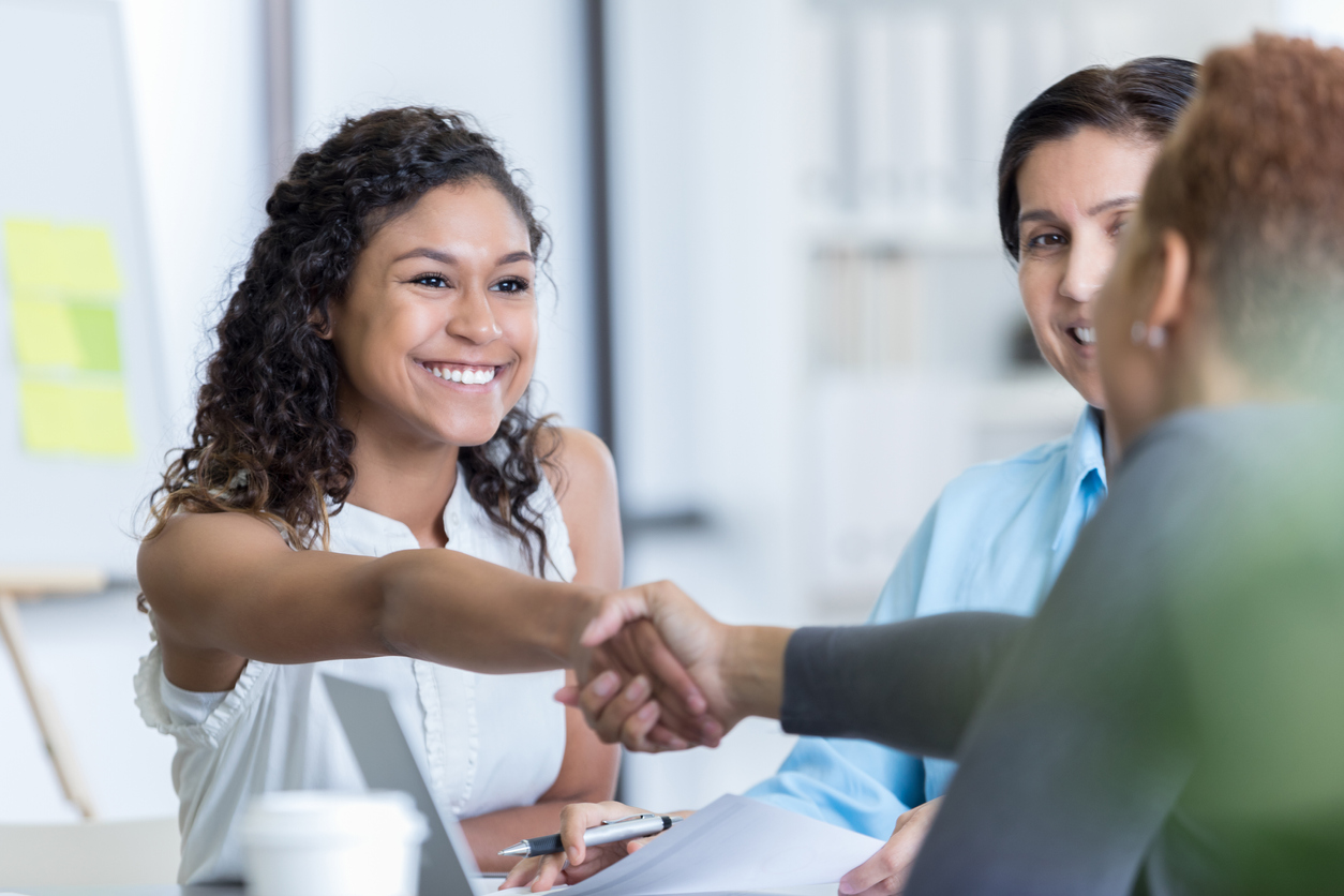 Confident young woman interviews for a position in an office. She is greeting the office manage. She is smiling confidently.