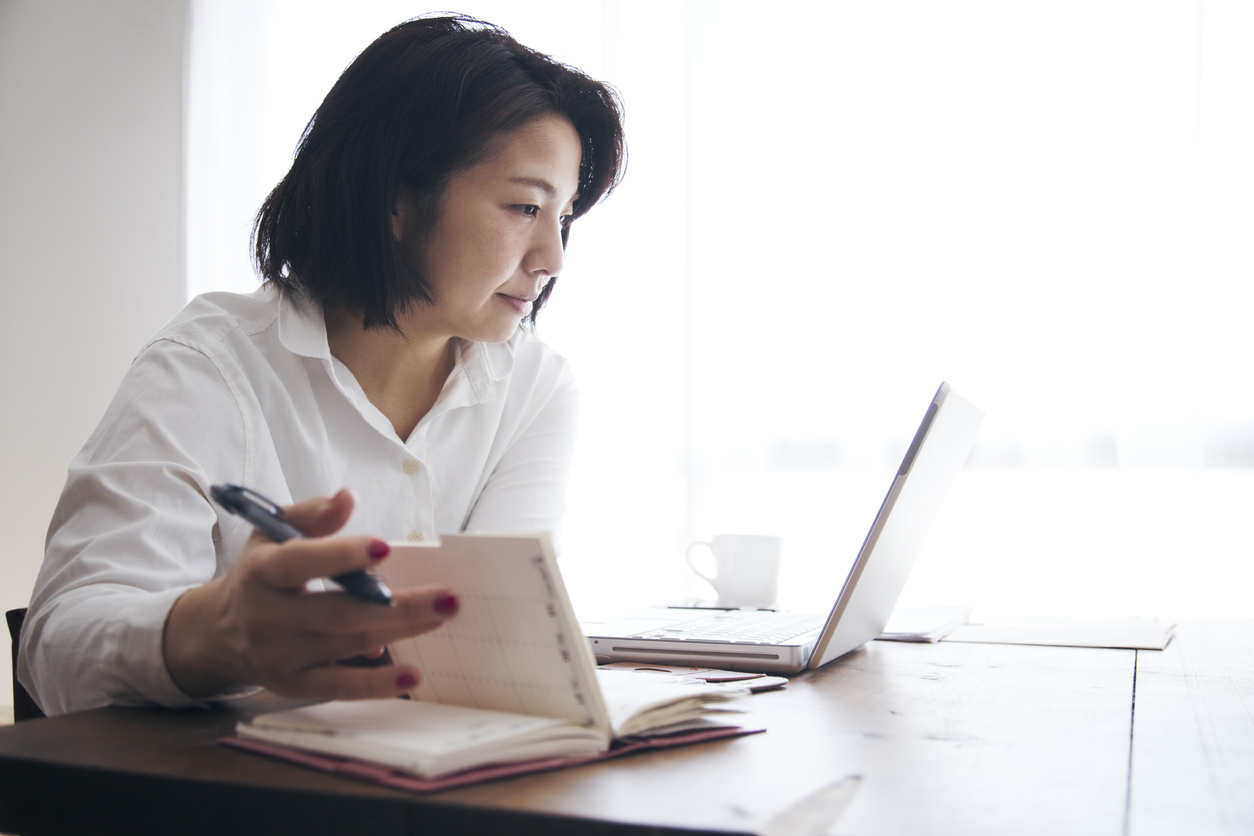 Japanese woman in casual clothes checking aa temporary placement agency online for an accounting job on a laptop.