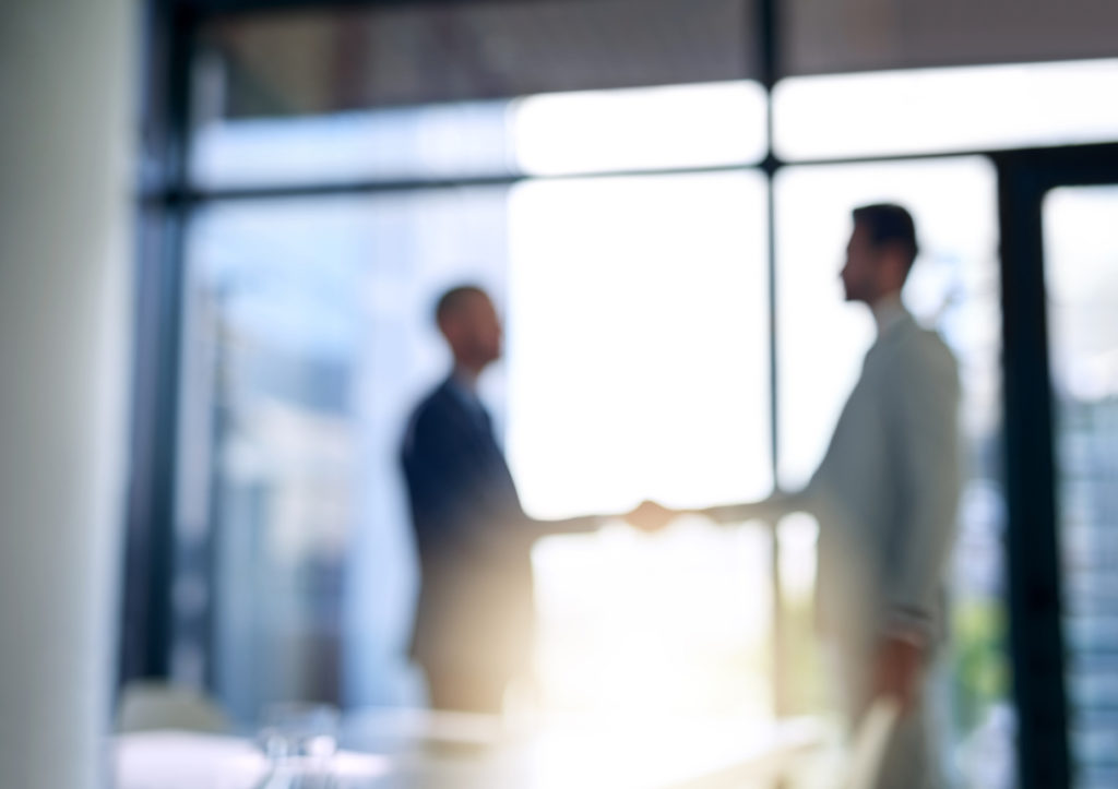 Blurred shot of two businessmen shaking hands in a modern office - staffing agency concept