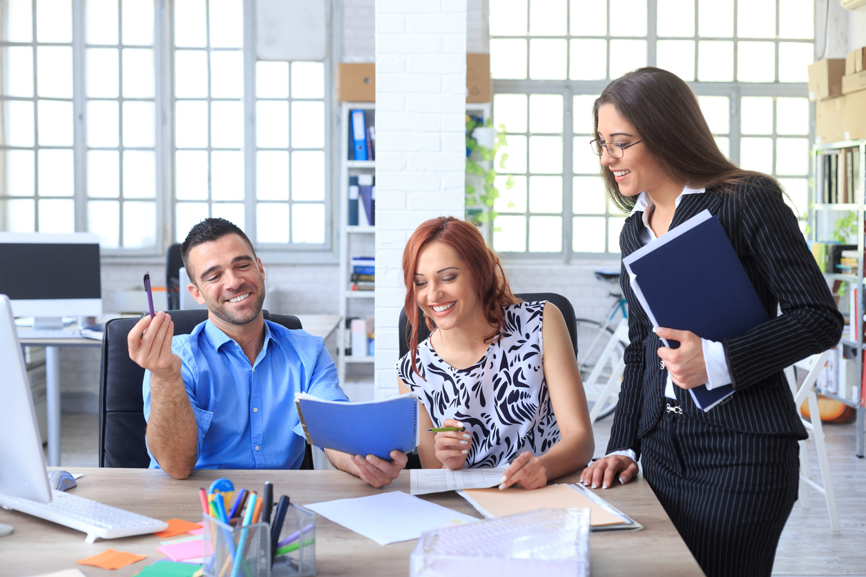 Business people looking at resumes from a temporary staffing agency. As background windows, shelves with boxes and folders. On desk monitor, tools and papers.