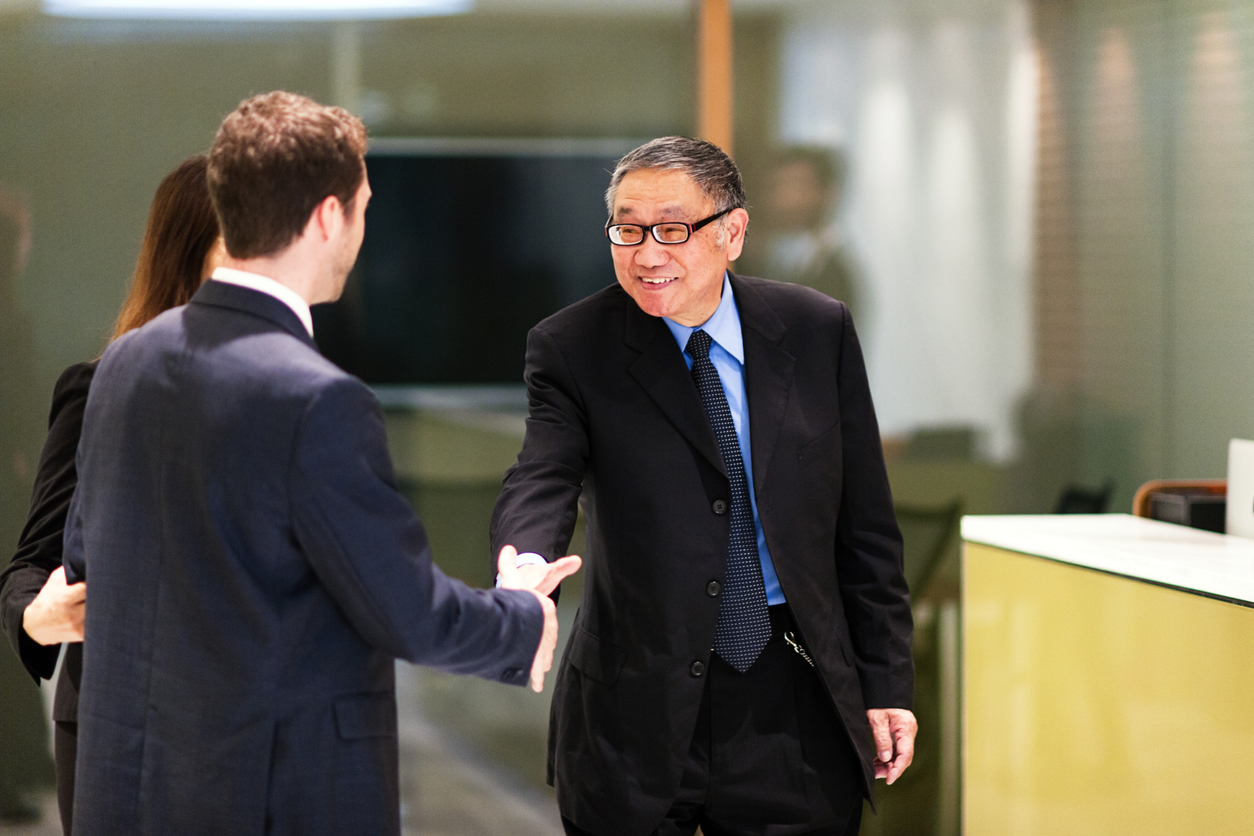Senior businessman using temp services to find new hires for his company. Shaking hands with potential new employee in the foyer of the office building.