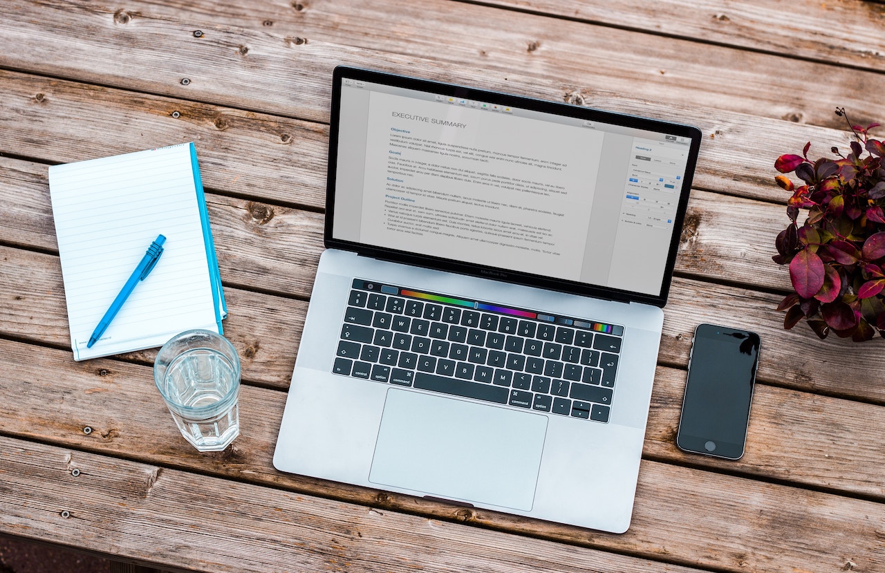 Notebook, glass, phone and laptop on a table. Resume is in the laptop screen