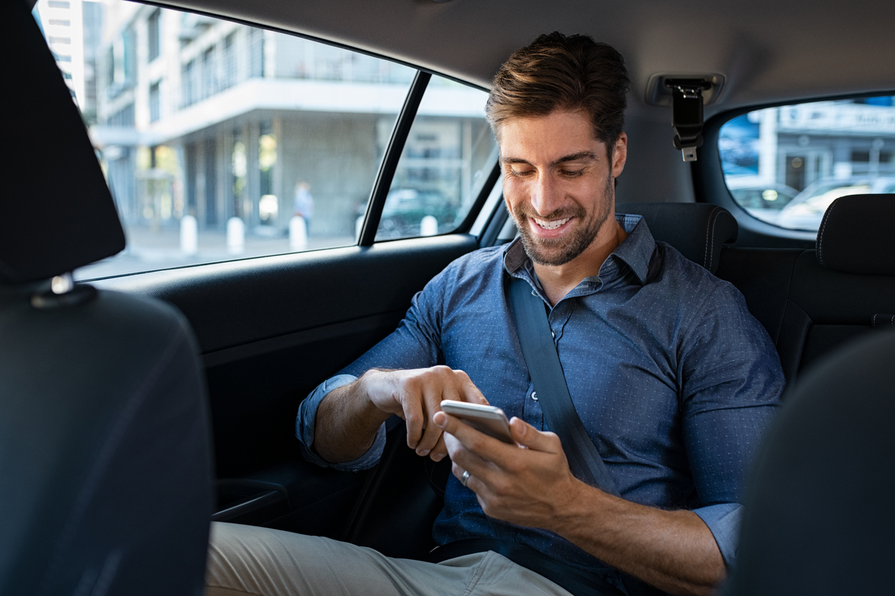 Happy smiling businessman man typing message on phone while sitting in a taxi. He is traveling for work in a career that require tons of travel