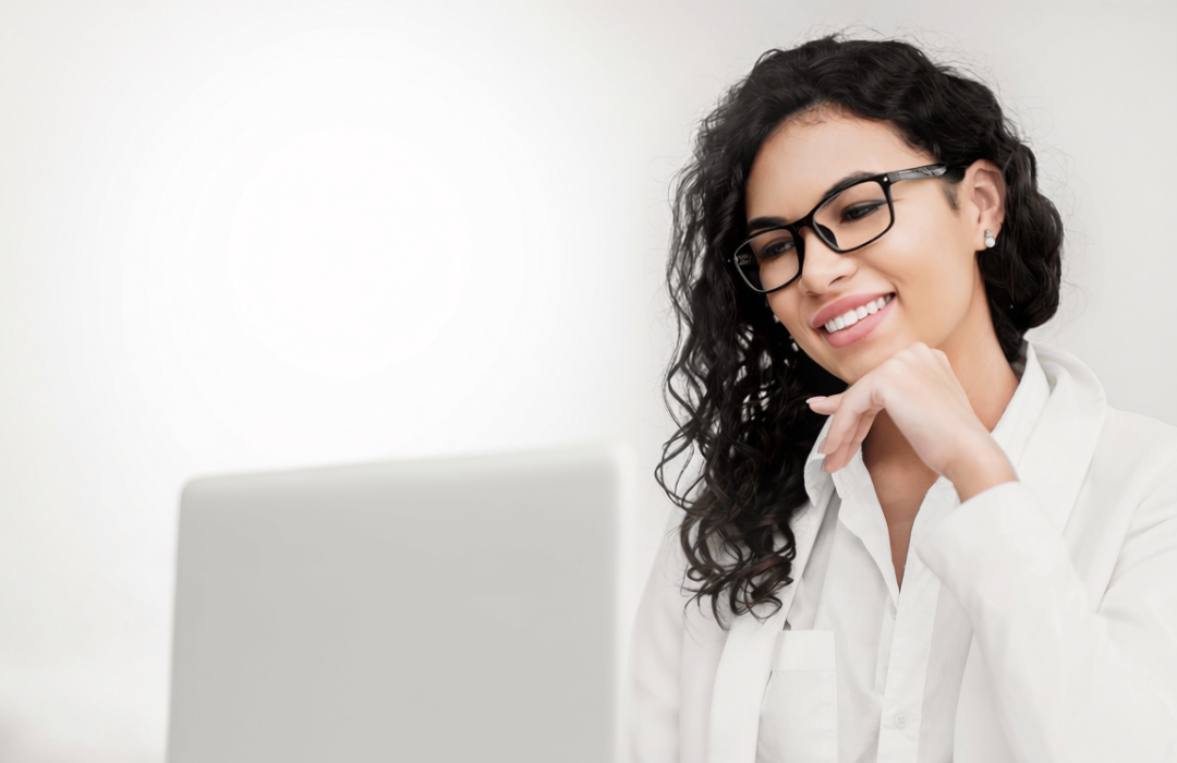 A woman is looking at her computer smiling, about to write a thank you letter to the hiring manager she just interviewed with.